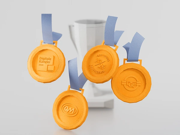 Vier orangefarbene Medaillen mit blauen Bändern hängen vor einem weißen Pokal. Die Medaillen sind beschriftet mit "Digitale Kanzlei 2023", einem Logo und weiteren Symbolen.
